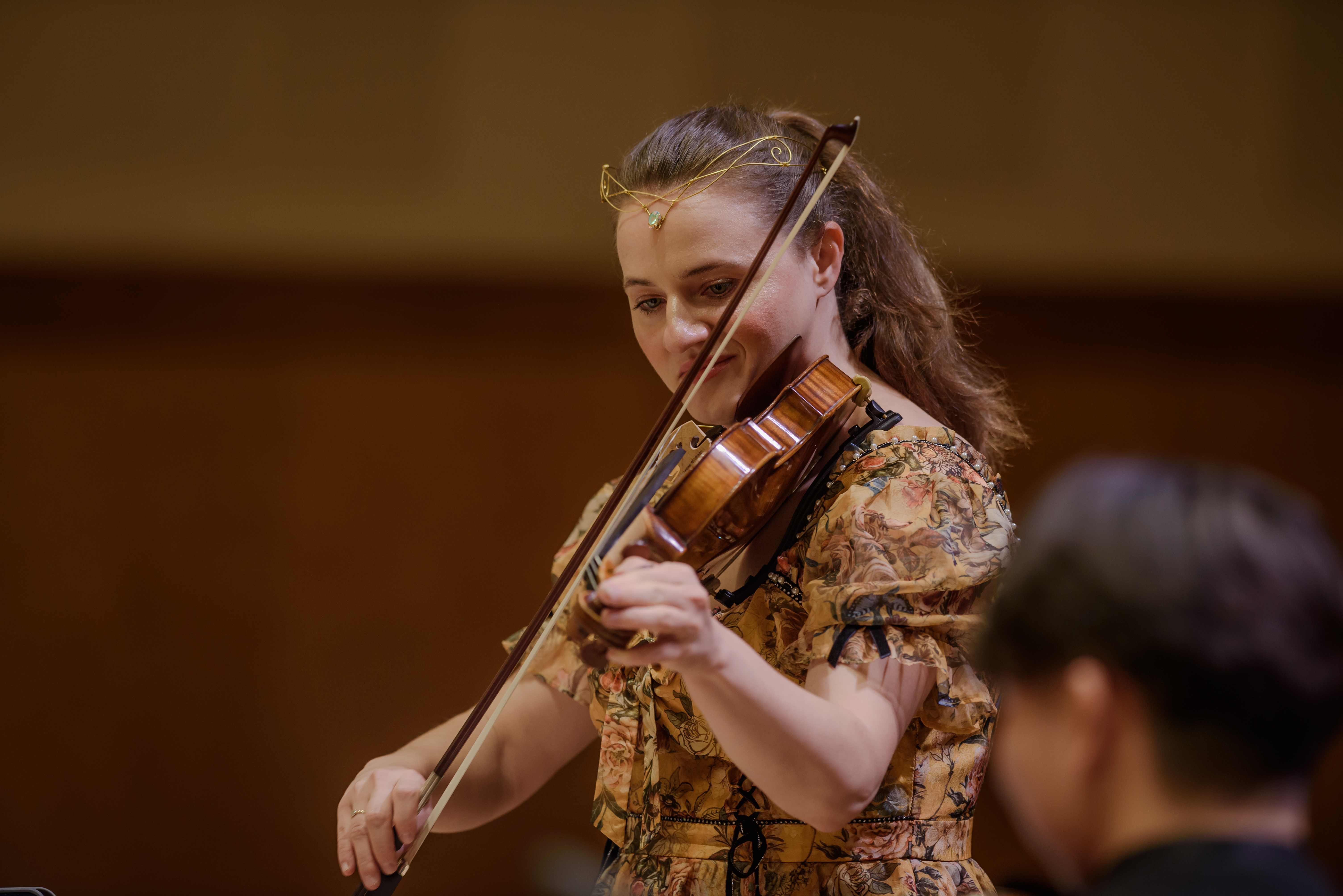 A guest soloist performing violin with the GG Orchestra in a warmly lit concert hall