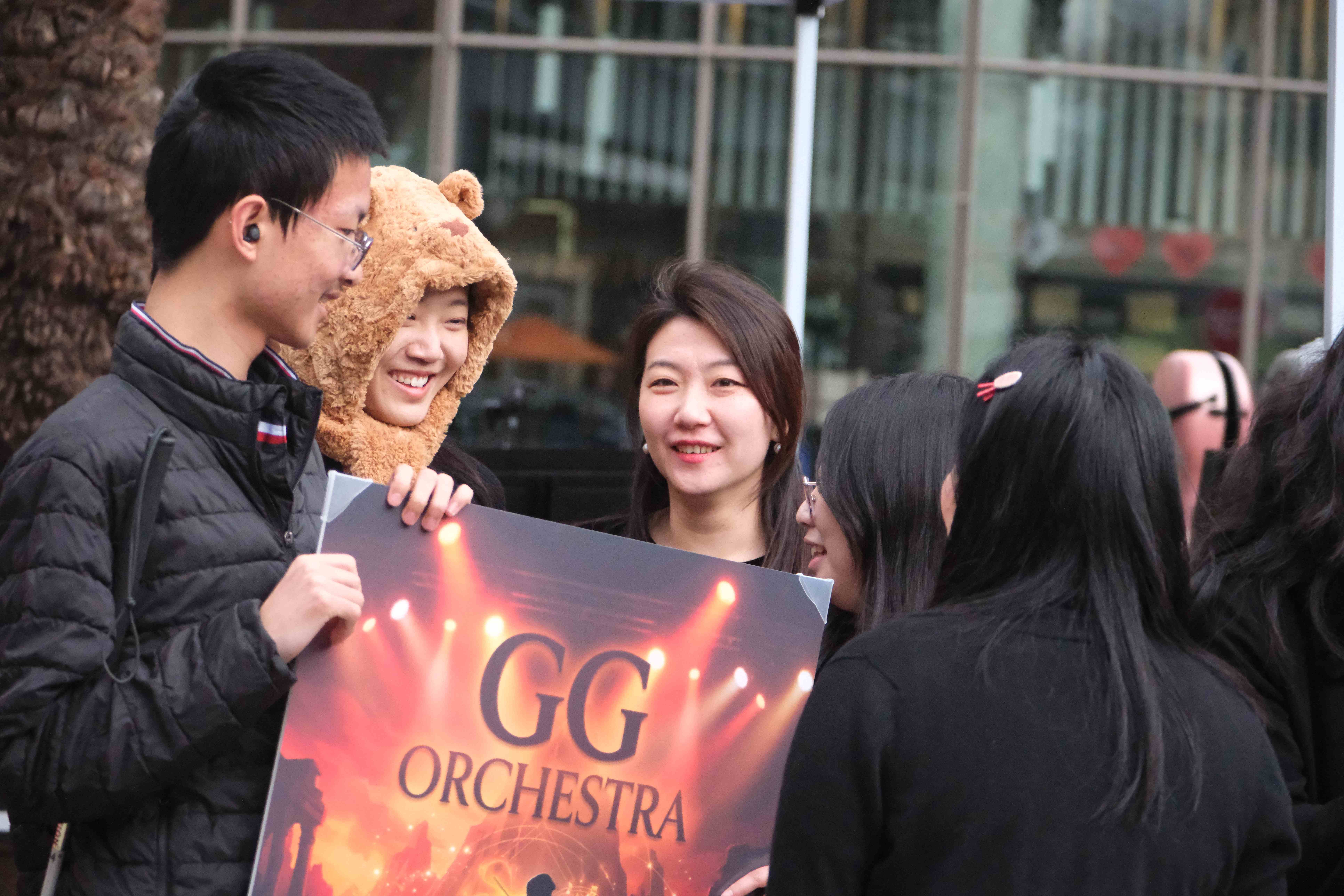 GG Orchestra members smiling and holding the GG Orchestra poster outdoors
