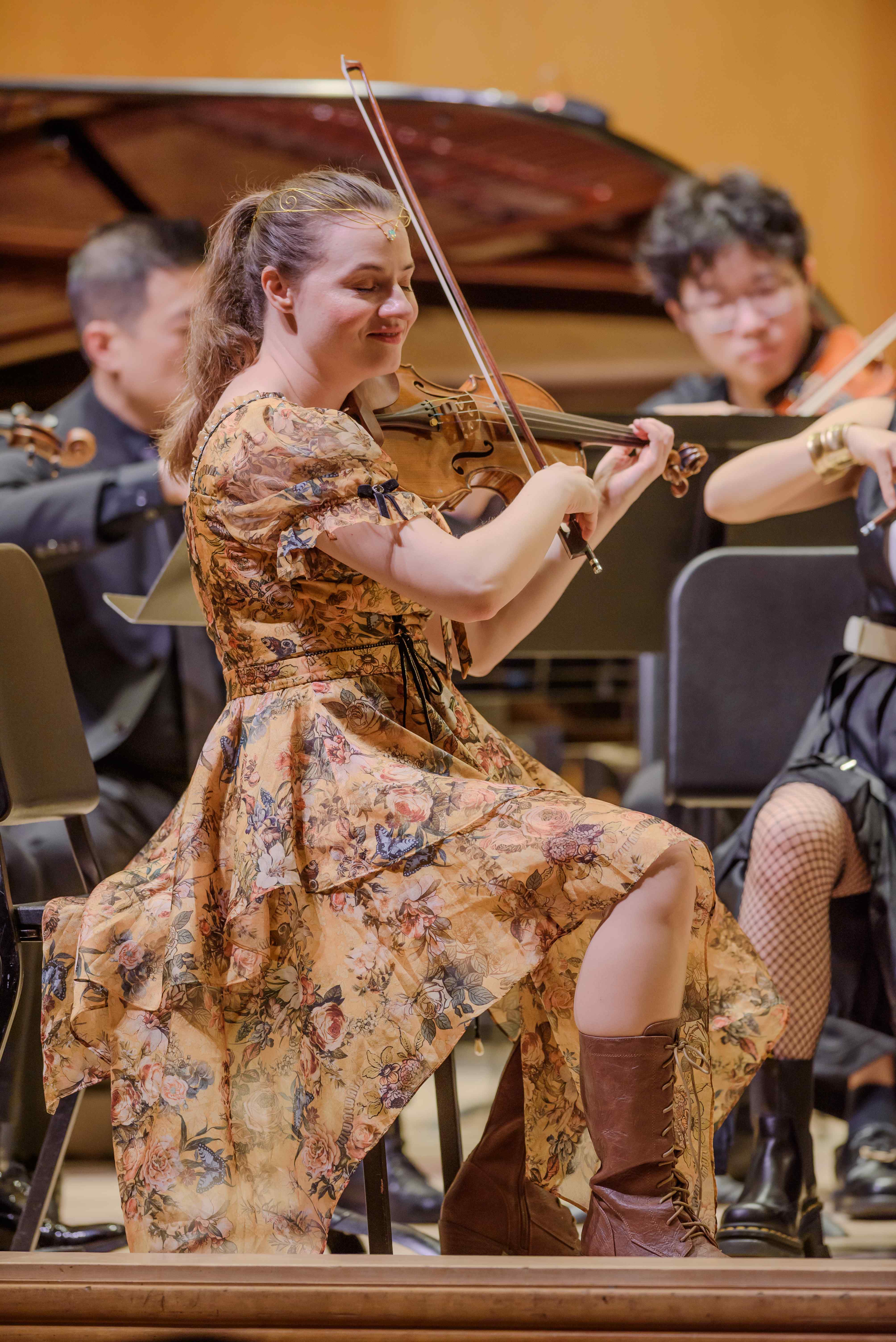 Violinist in a floral dress smiling while performing with the ensemble